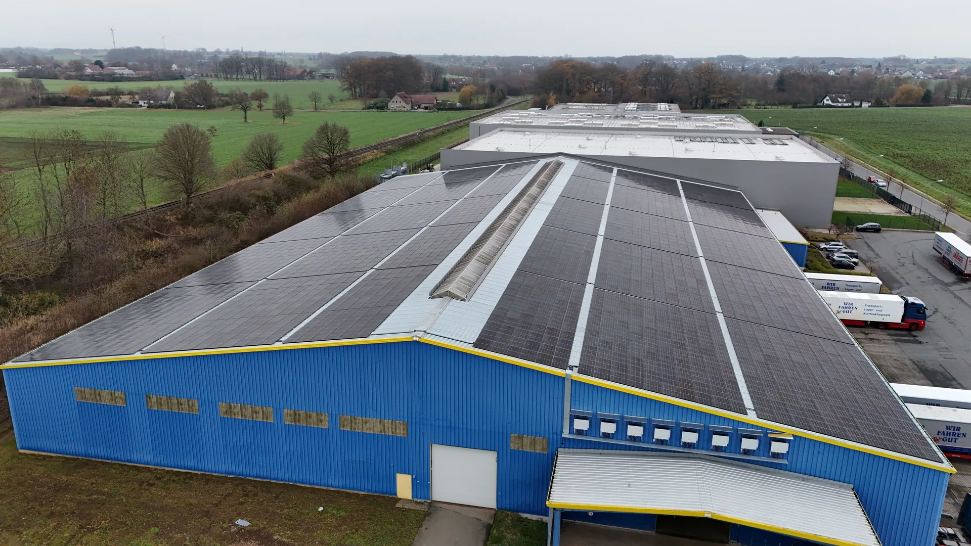 Südwestansicht des Logistikgebäudes – vollständig bestücktes Hallendach, blau-gelbe Fassade, ländliche Umgebung